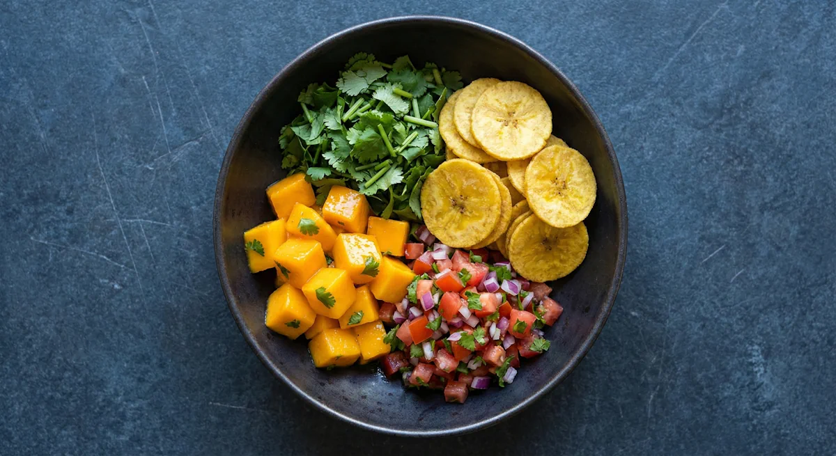 Frische Mango-Tomaten-Salsa mit Koriander, serviert mit einer Handvoll knuspriger Kochbananenchips in einer dunklen Schale.