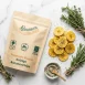 Stapel knusprige Kochbananenchips mit Alpenkräutersalz, umgeben von frischen Rosmarin- und Thymianzweigen auf hellem Marmor – Premium-Snack aus lokaler Zürcher Produktion.